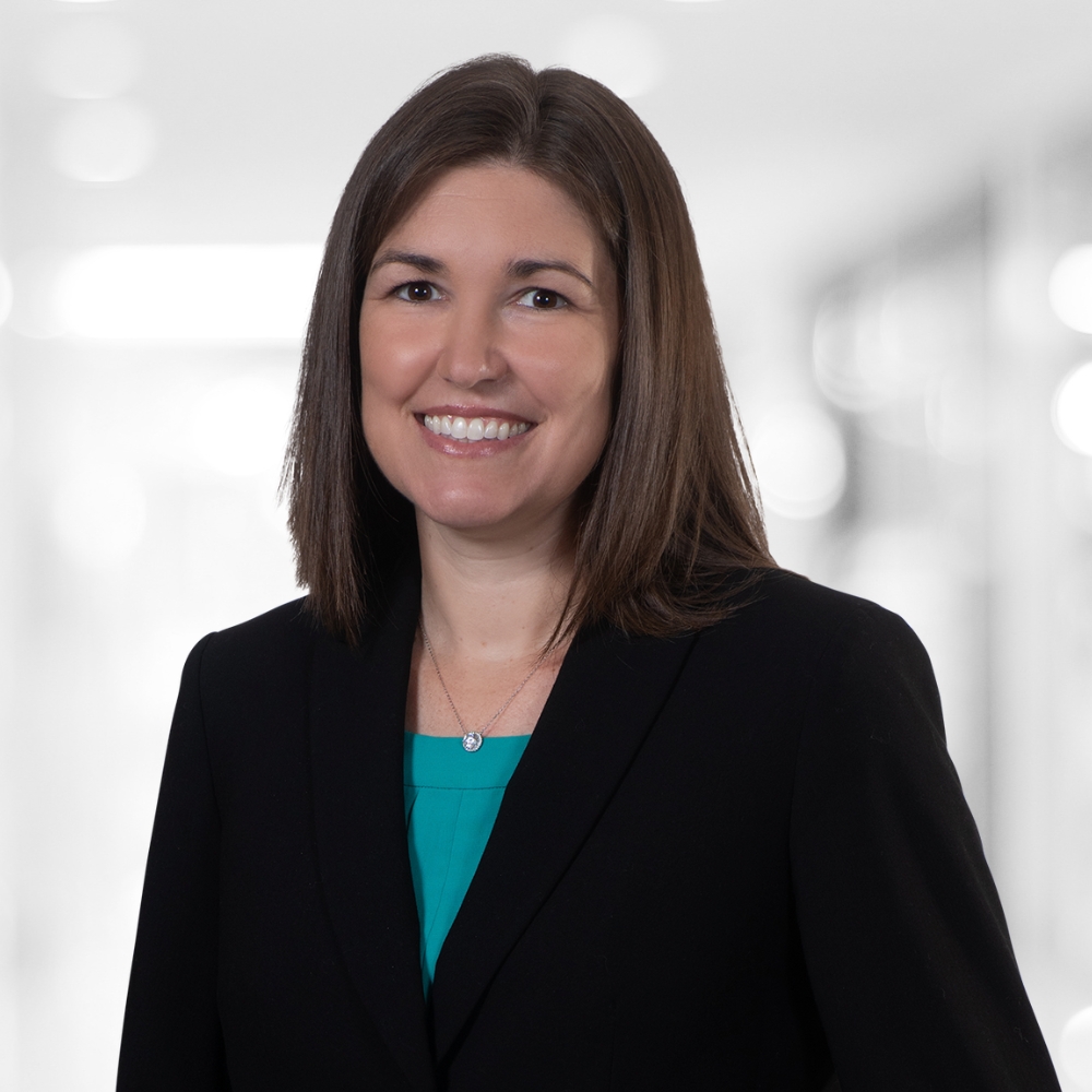 Puopolo Woman with straight brown hair wearing a black blazer and teal top, posing in a softly blurred indoor professional setting.